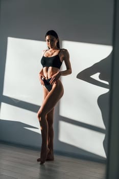In black underwear. Young caucasian woman with slim body shape is indoors at daytime.