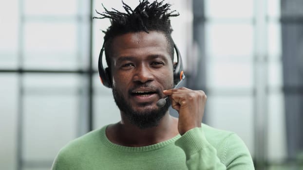 Operator of hot line. Portrait of cheerful african customer service representative with headset in call center, empty space