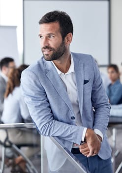 A portrait of a young businessman looking through the window during a meeting and presentation in the office. Business concept