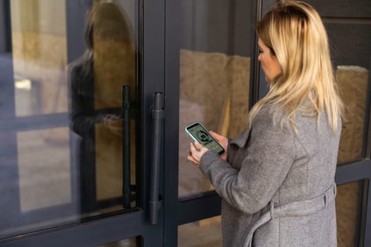Close-up of woman standing near the wooden door and locking it with online application on her smartphone