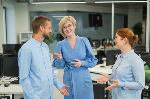Colleagues communicate at work. Red-haired woman, blonde and bearded man in a denim shirt in the office