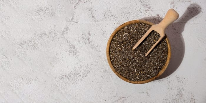 Chia seeds in wooden bowl with wooden spoon. Healthy superfood rich in Omega 3 fatty acids. Dry healthy natural ingredient. Chia grains are falling. Vegetarian food