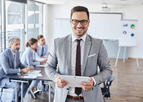 A portrait of a young smiling businessman holding a tablet during a meeting and presentation in the office. Business concept