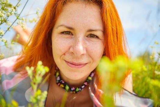 Outdoors portrait of red haired woman in grass and lower on field and meadow. Young woman enjoying her freedom in flowering nature