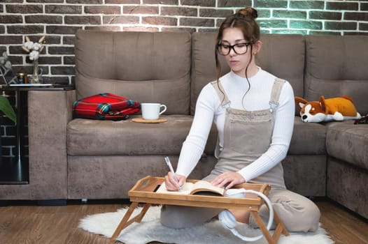 Talented caucasian young woman draws a design sketch in a notebook while enjoying her favorite hobby in home interior. Thoughtful hipster girl writing down notes on future plans in a notebook.
