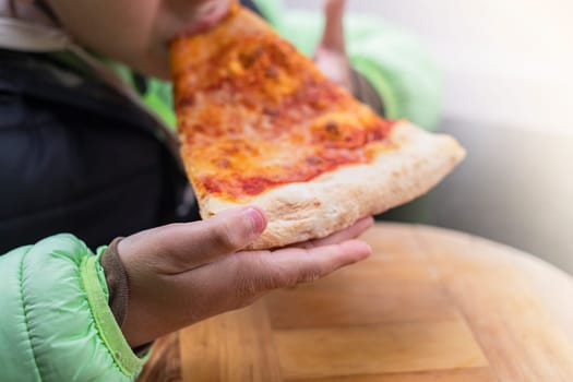 Boy eating a piece of pizza on wooden background in outdoor. Lifestyle