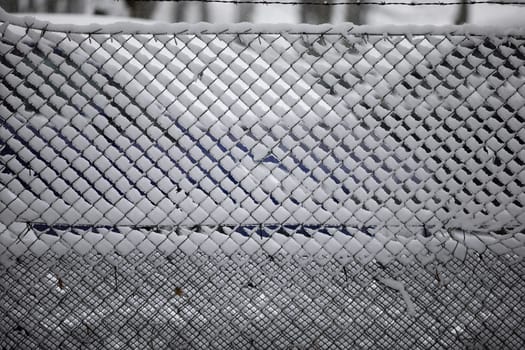 Snow has settled on a wire fence. Close-up of a frozen fence covered with snow. The spaces between the wire are filled with snow and ice.