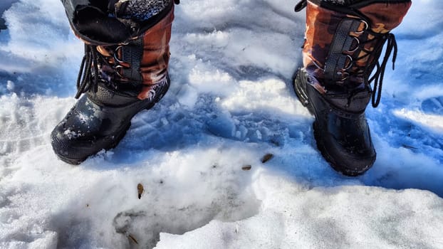 Feet of Hunter or fisherman in big warm boots on a winter day on snow. Top view. A fisherman on the ice of river, lake, reservoir on a spring day with melting ice. Dangerous fishing