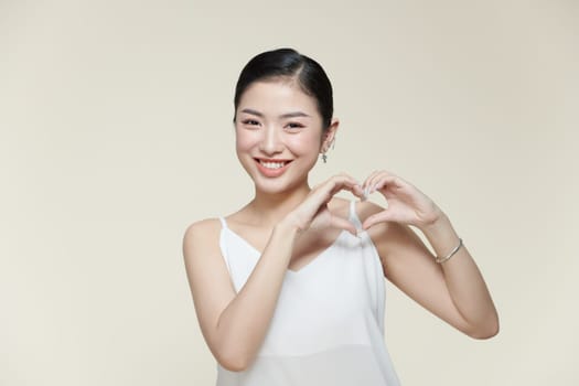 Portrait of positive young lady with healthy smooth skin holding hands in the shape of a heart near face