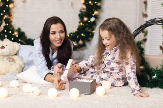 Pretty smiling child girl with mother opening magical box with Christmas gift at home
