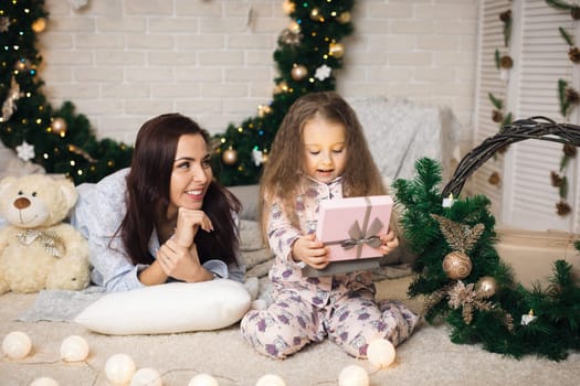 Pretty smiling child girl with mother opening magical box with Christmas gift at home