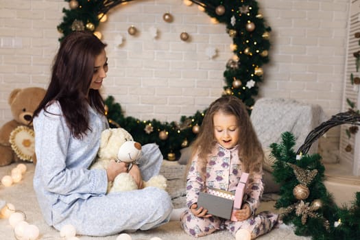 Pretty smiling child girl with mother opening magical box with Christmas gift at home