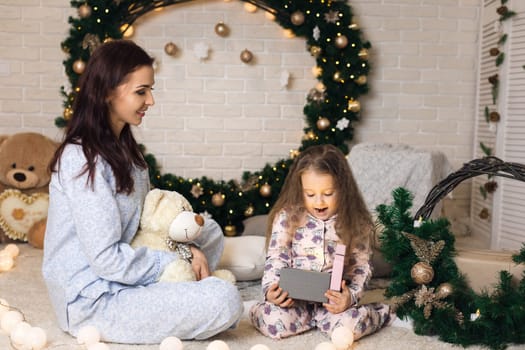 Pretty smiling child girl with mother opening magical box with Christmas gift at home