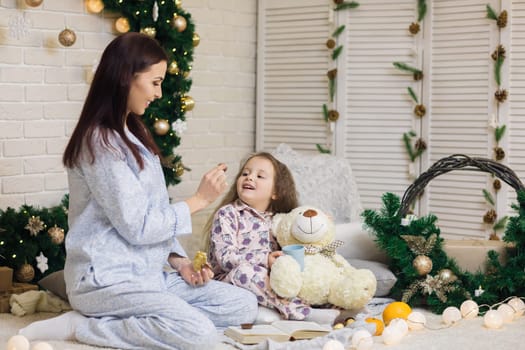 Cute smiling child girl with her mother play with teddy bear at home. Christmas