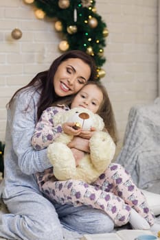 happy mother with her little child daughter playing near the Christmas tree