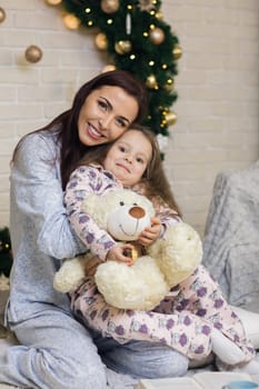 happy mother with her little child daughter playing near the Christmas tree