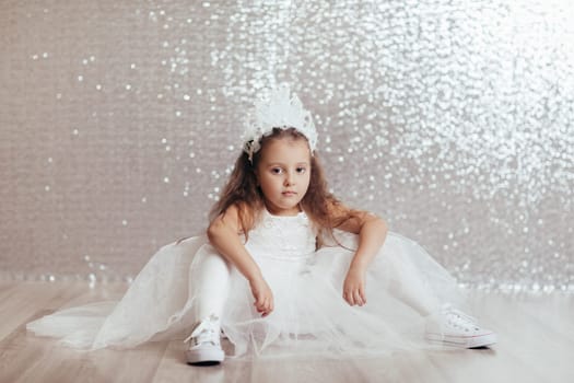 sad little child girl in blue dress sitting on the floor with confetti on background with silver bokeh. after birtday party