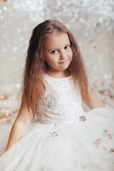 portrait of beautiful smiling little child girl in silver and blue dress on background with silver bokeh. birtday party