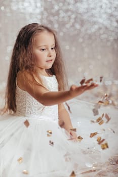 portrait of beautiful smiling little child girl in silver and blue dress on background with silver bokeh. birtday party