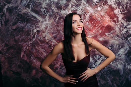 Portrait of magnificent sexy woman in evening dress posing over dark red background