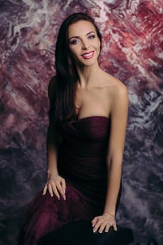 Portrait of magnificent sexy woman in evening dress posing over dark red background