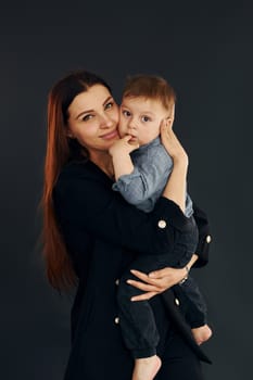 Mother in stylish black clothes is with her little son in the studio.