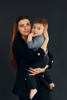 Mother in stylish black clothes is with her little son in the studio.