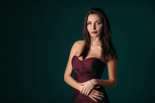 Portrait of magnificent sexy woman in evening dress posing over dark green background