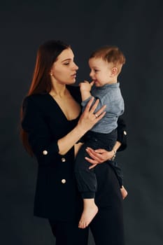 Mother in stylish black clothes is with her little son in the studio.