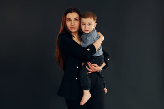 Mother in stylish black clothes is with her little son in the studio.