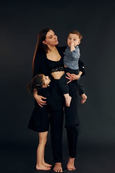 Woman in black stylish clothes is with her little son and daughter in the studio.