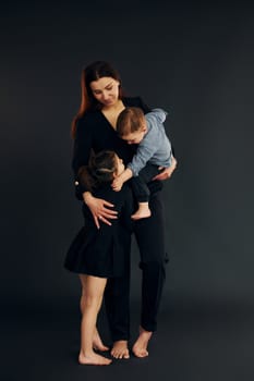 Woman in black stylish clothes is with her little son and daughter in the studio.