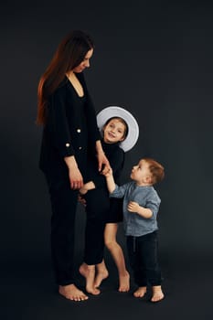 Woman in black stylish clothes is with her little son and daughter in the studio.