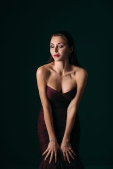 Portrait of magnificent sexy woman in evening dress posing over dark green background