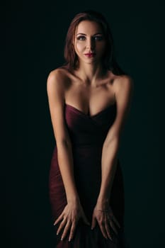 Portrait of magnificent sexy woman in evening dress posing over dark green background