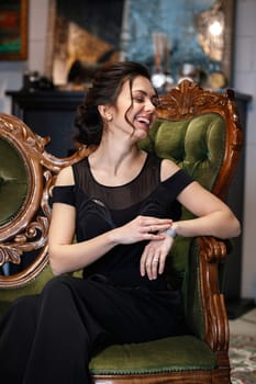 elegant smiling brunette woman with hairstyle in black clothes sits on a sofa