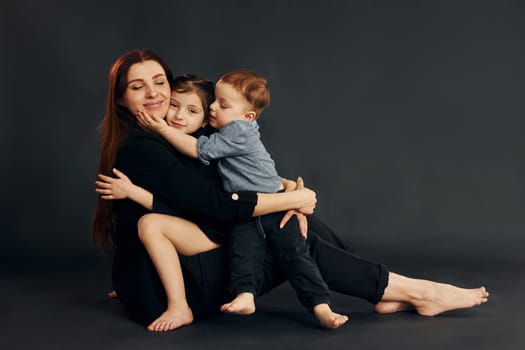 Woman in black stylish clothes is with her little son and daughter in the studio.