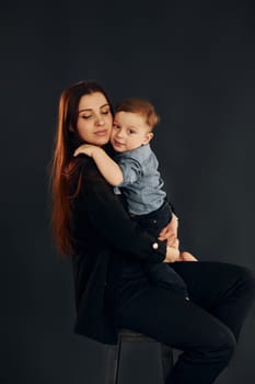 Mother in stylish black clothes is with her little son in the studio.