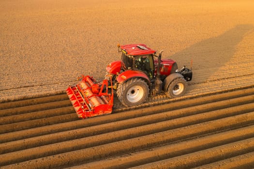 PRAGUE , CZECH REPUBLIC - MARCH 18 2022: Heavy tractor prepares soil making beds for planting in rural field. Agricultural machine operates at sunset in countryside aerial view