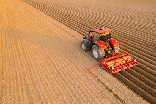 PRAGUE , CZECH REPUBLIC - MARCH 18 2022: Contemporary tractor drags plug making furrows on soil in field. Heavy vehicle helps with agricultural process at sunset in countryside aerial view