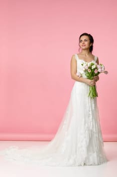 beautiful bride with wedding bouquet of pink tulips on pink background
