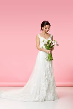 beautiful bride with wedding bouquet of pink tulips on pink background