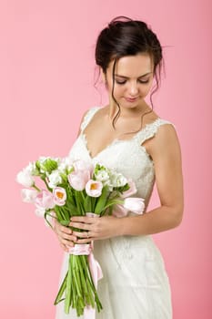 beautiful bride with wedding bouquet of pink tulips on pink background