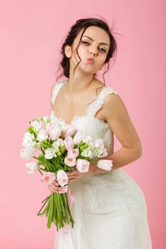 beautiful bride with wedding bouquet of pink tulips on pink background