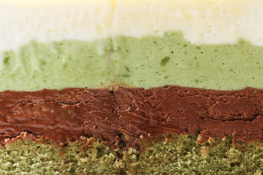 Close-up cut of pistachio mousse cake. Pistachio sponge cake filling, pistachio mousse, chocolate mousse and white chocolate mousse.