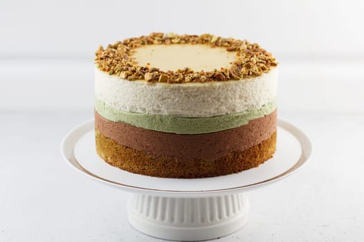 Pistachio cake on a stand on a gray background. Ingredients: pistachio sponge cake, pistachio mousse, chocolate mousse and white chocolate mousse