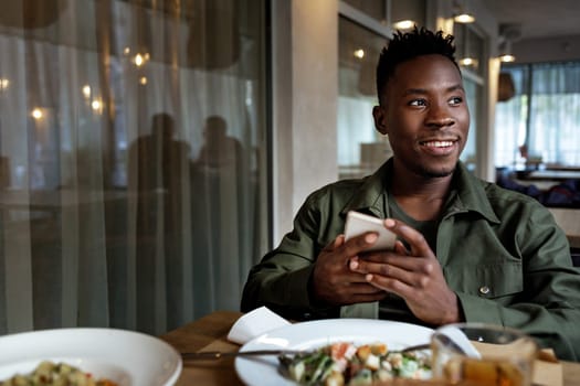 young smiling african american man messaging online, checking social networks in cafe. copy space