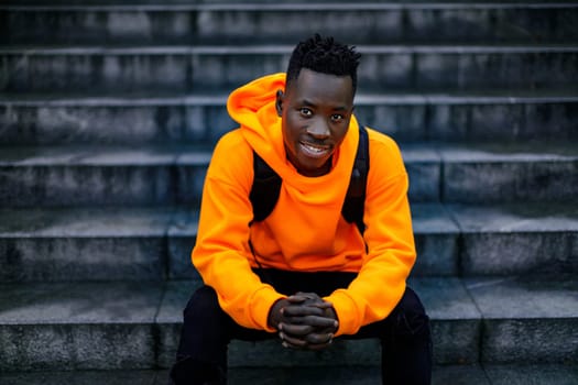 african-american man in stylish orange hoodie sweatshirt sitting on stairs