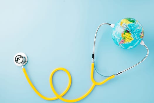 World Health Day Concept. Top view yellow doctor stethoscope and world globe isolated on pastel blue background with copy space, Save world day, Environment Green Earth, Health care and medical