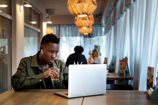 Cheerful young african american man in headphones using computer in cafe